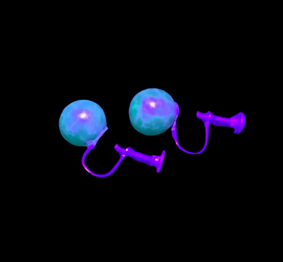 Green glowing earrings under a black light on a dark surface