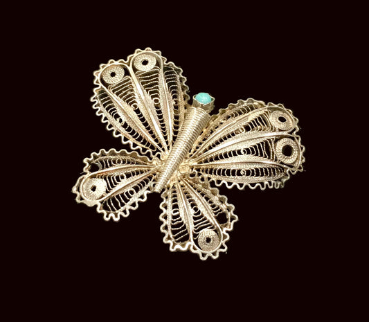 Silver butterfly brooch with turquoise center on a black background