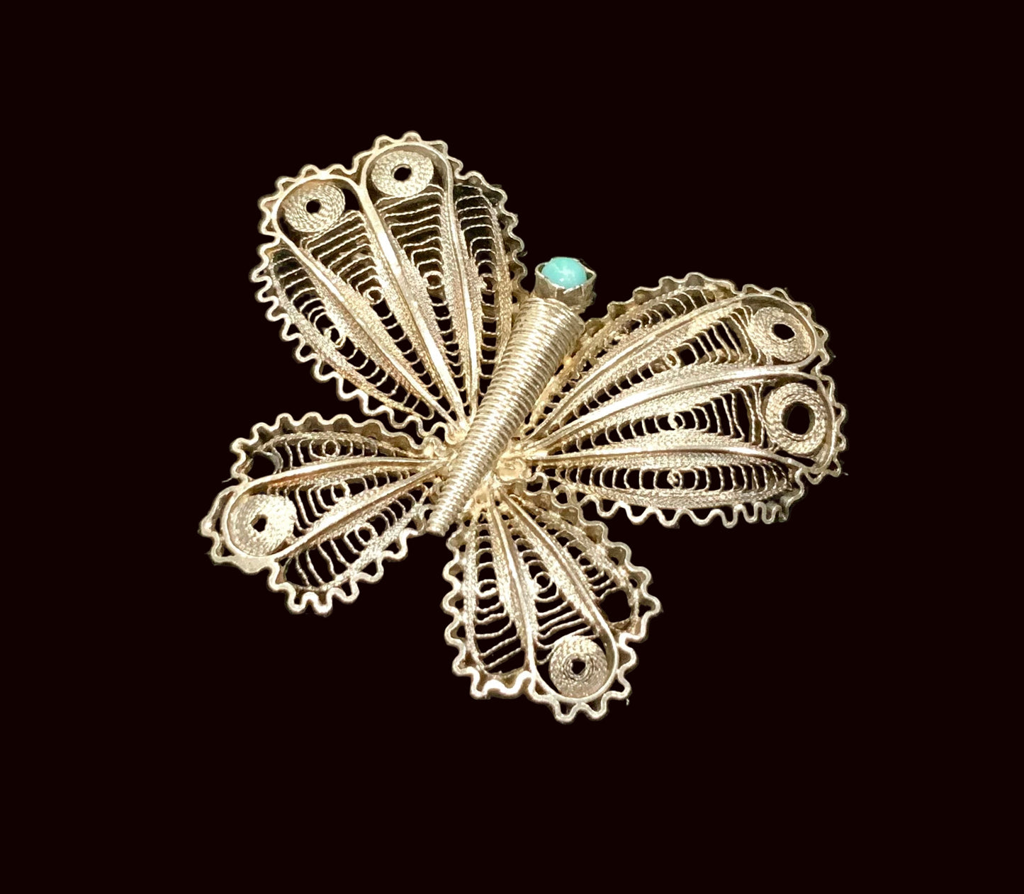 Silver butterfly brooch with turquoise center on a black background