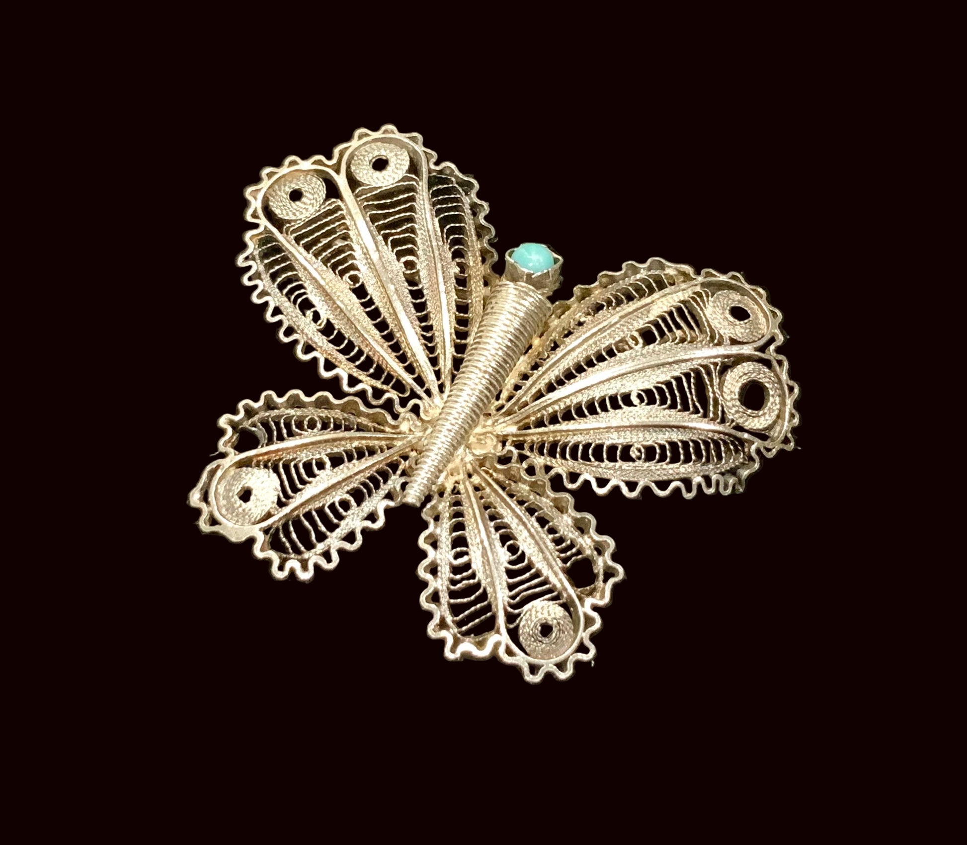 Silver butterfly brooch with turquoise center on a black background