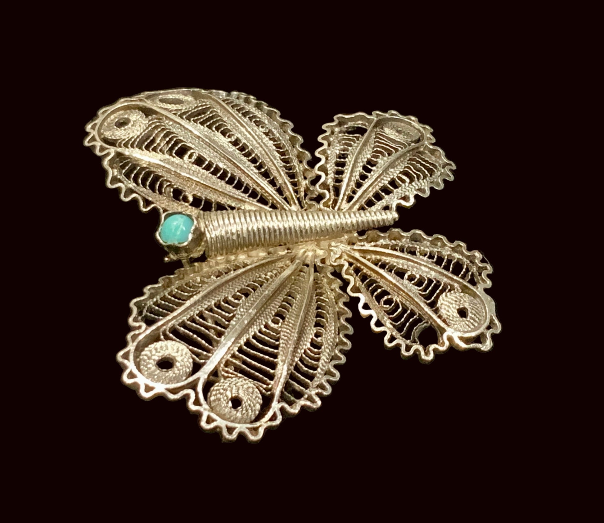 Silver butterfly brooch with turquoise center on a black background