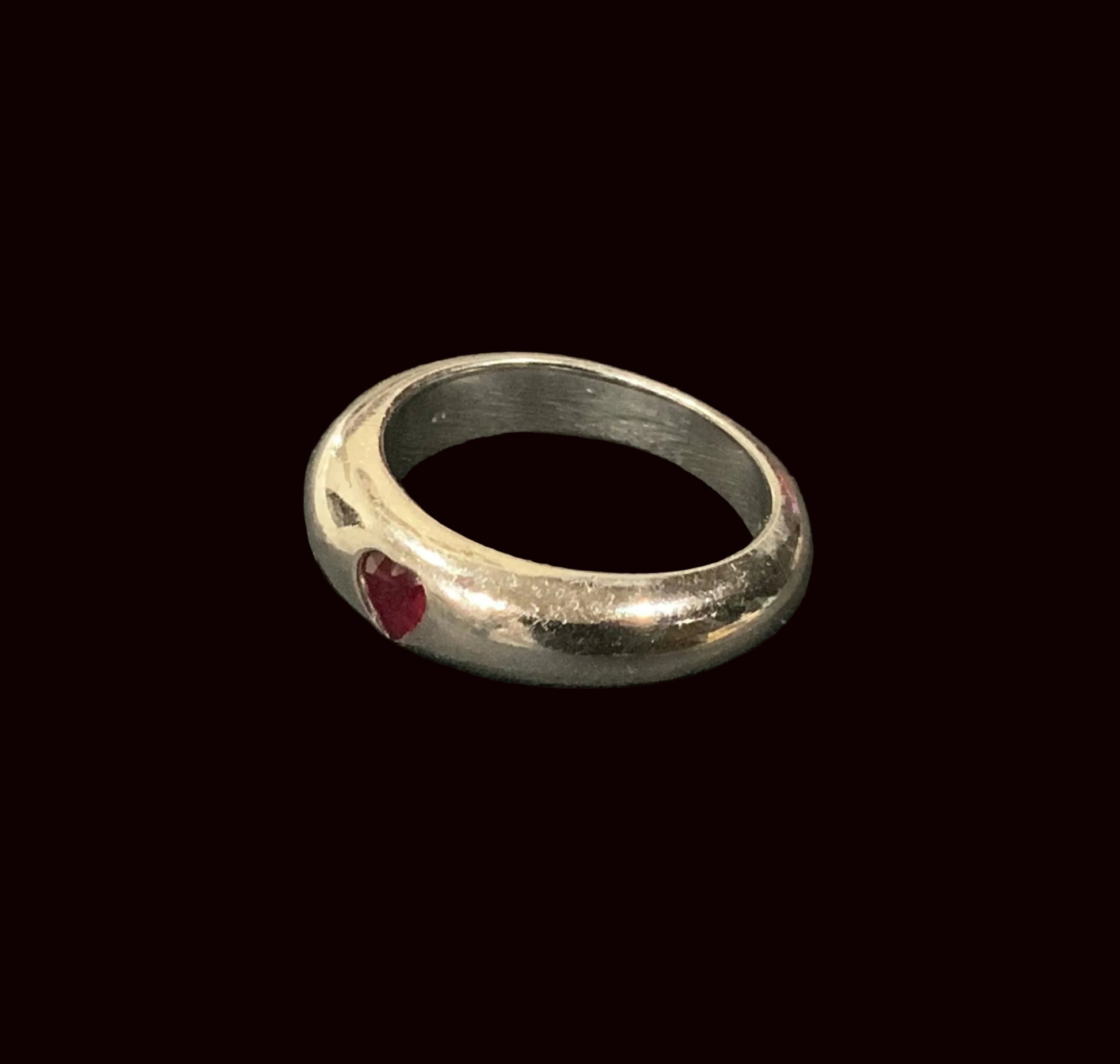 Silver ring with a red gemstone on a black leather surface