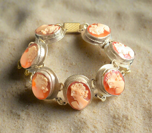 A silver bracelet featuring a series of hand-carved shell cameos in red color, displayed on a sandy surface.